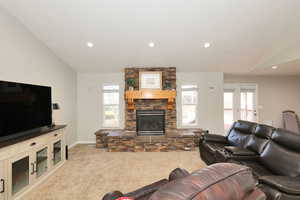 Living room with light colored carpet, a stone fireplace, recessed lighting, and lofted ceiling