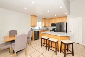 Kitchen with black appliances, a breakfast bar area, light tile patterned flooring, recessed lighting, and light stone counters
