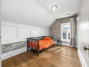 Bedroom with wood finished floors, vaulted ceiling, and brick wall
