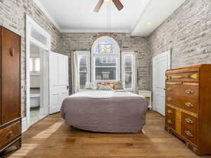 Bedroom featuring crown molding, wood finished floors, ceiling fan, and brick wall