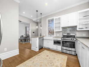 Kitchen featuring crown molding, open shelves, white cabinets, stainless steel appliances, and hanging light fixtures