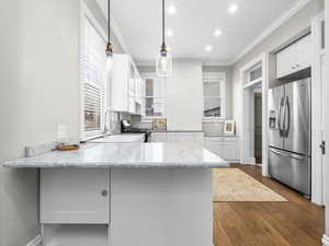 Kitchen with light stone countertops, a peninsula, white cabinets, appliances with stainless steel finishes, and ornamental molding