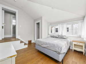 Bedroom featuring multiple windows, light wood-type flooring, and vaulted ceiling