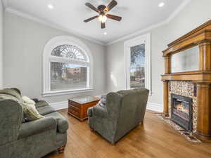 Living room with ornamental molding, light wood finished floors, a ceiling fan, a tile fireplace, and recessed lighting