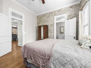 Bedroom with ornamental molding, multiple windows, wood finished floors, a ceiling fan, and brick wall