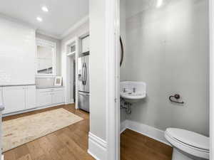 Half bath with light wood-style floors, crown molding, tasteful backsplash, and recessed lighting