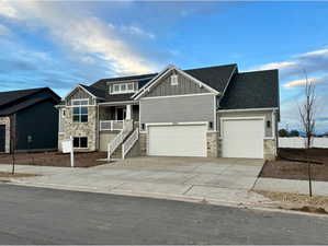 Craftsman-style house featuring board and batten siding, stone siding, driveway, and roof with shingles