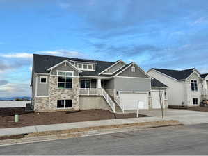 Craftsman inspired home featuring stone siding, board and batten siding, driveway, a shingled roof, and covered porch