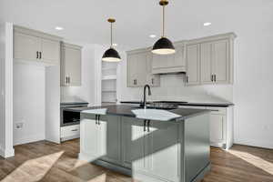Kitchen featuring dark countertops, decorative backsplash, an island with sink, dark wood finished floors, and custom range hood
