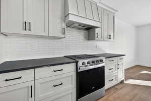 Kitchen featuring stainless steel gas range, premium range hood, light wood-type flooring, decorative backsplash, and white cabinetry