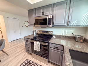 Kitchen featuring stainless steel appliances, gray cabinets, dark stone counters, and light wood finished floors
