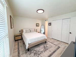 Bedroom with light wood-style floors, multiple windows, and a closet