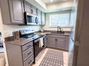Kitchen featuring stainless steel appliances, gray cabinetry, dark stone countertops, recessed lighting, and light wood-style floors