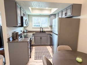 Kitchen with gray cabinetry, a raised ceiling, stainless steel appliances, dark stone counters, and light wood-type flooring