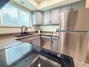 Kitchen with appliances with stainless steel finishes, gray cabinetry, and dark stone counters
