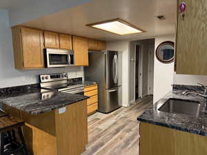 Kitchen with dark stone countertops, a peninsula, appliances with stainless steel finishes, light wood finished floors, and brown cabinets