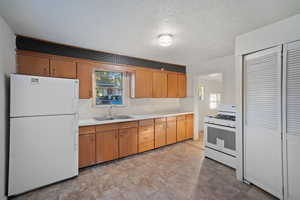 Kitchen featuring light countertops, white appliances, brown cabinetry, and a textured ceiling