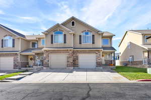 View of front facade with stone siding, driveway, a garage, and stucco siding