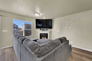 Living room with a warm lit fireplace, a textured ceiling, and wood finished floors