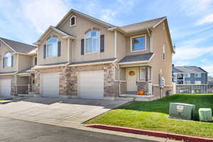 View of front facade with driveway, stucco siding, a front yard, an attached garage, and stone siding