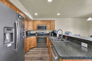 Kitchen featuring appliances with stainless steel finishes, dark countertops, a peninsula, dark wood-type flooring, and recessed lighting