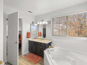 Ensuite bathroom with a tub with jets, vanity, and light wood finished floors