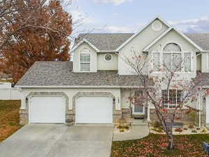 View of front of house featuring roof with shingles, a garage, driveway, brick siding, and stucco siding
