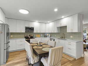 Kitchen featuring stainless steel appliances, white cabinetry, light wood finished floors, decorative backsplash, and recessed lighting