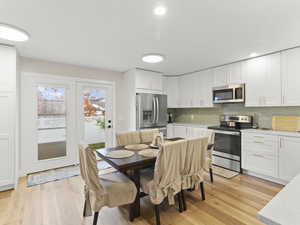 Kitchen featuring stainless steel appliances, white cabinetry, decorative backsplash, light wood-style flooring, and light stone countertops
