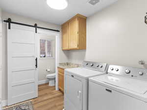 Laundry area featuring light wood-type flooring, washing machine and dryer, and a barn door