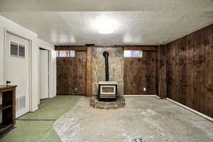 Unfurnished living room featuring a wood stove, wood walls, and a textured ceiling