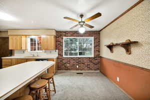 Kitchen featuring light countertops, ornamental molding, light carpet, a breakfast bar, and a ceiling fan