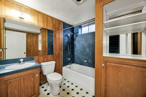 Full bathroom featuring wooden walls, vanity,  shower combination, and a textured ceiling