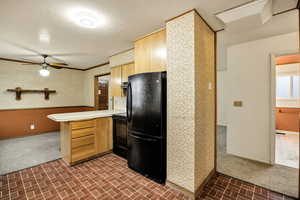 Kitchen with wallpapered walls, light countertops, brick patterned floors, a peninsula, and black appliances