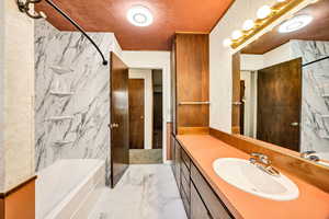 Bathroom featuring a combined bath / shower with marble appearance, light marble finish floors, vanity, and tile walls