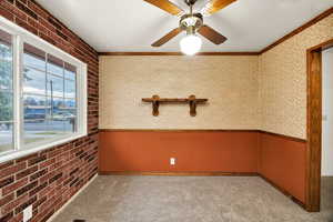 Spare room with crown molding, carpet flooring, ceiling fan, brick wall, and a wainscoted wall