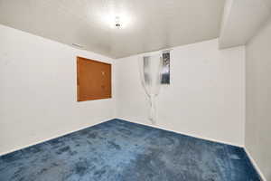 Carpeted spare room featuring a textured ceiling and baseboards