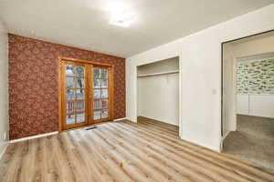 Unfurnished bedroom featuring french doors, light wood-style floors, wallpapered walls, a textured ceiling, and a closet