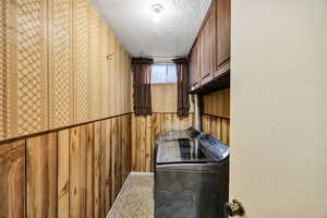 Laundry room featuring a textured ceiling, independent washer and dryer, cabinet space, and wallpapered walls