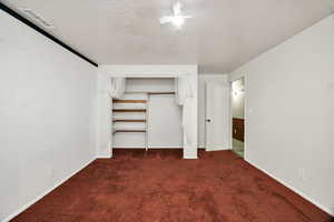 Unfurnished bedroom featuring dark carpet, a textured ceiling, a closet, and a ceiling fan