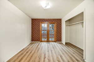 Unfurnished bedroom featuring french doors, light wood-style flooring, a closet, and a textured ceiling