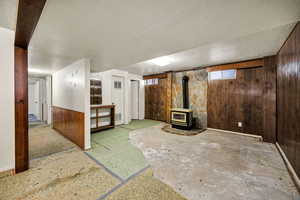Below grade area featuring wood walls, a wood stove, a textured ceiling, wainscoting, and a baseboard heating unit