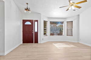 Entrance foyer featuring light wood-type flooring, a textured ceiling, a chandelier, and ceiling fan