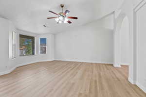 Unfurnished room featuring light wood-type flooring, a ceiling fan, and arched walkways