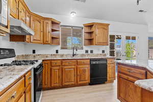 Kitchen with black appliances, light wood-style floors, brown cabinets, light stone counters, and healthy amount of natural light
