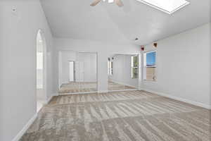 Unfurnished living room with carpet, ceiling fan, vaulted ceiling, a skylight, and arched walkways
