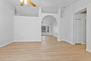 Spare room featuring light wood-type flooring, arched walkways, ceiling fan, and vaulted ceiling
