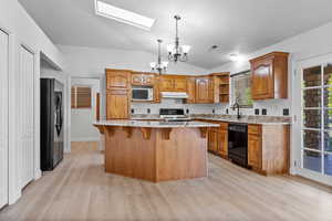 Kitchen with brown cabinets, a skylight, light stone counters, a chandelier, and lofted ceiling