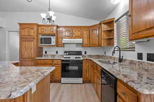 Kitchen with brown cabinetry, gas stove, vaulted ceiling, open shelves, and light stone counters