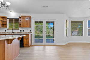 Kitchen featuring brown cabinets, french doors, light stone countertops, healthy amount of natural light, and a textured ceiling